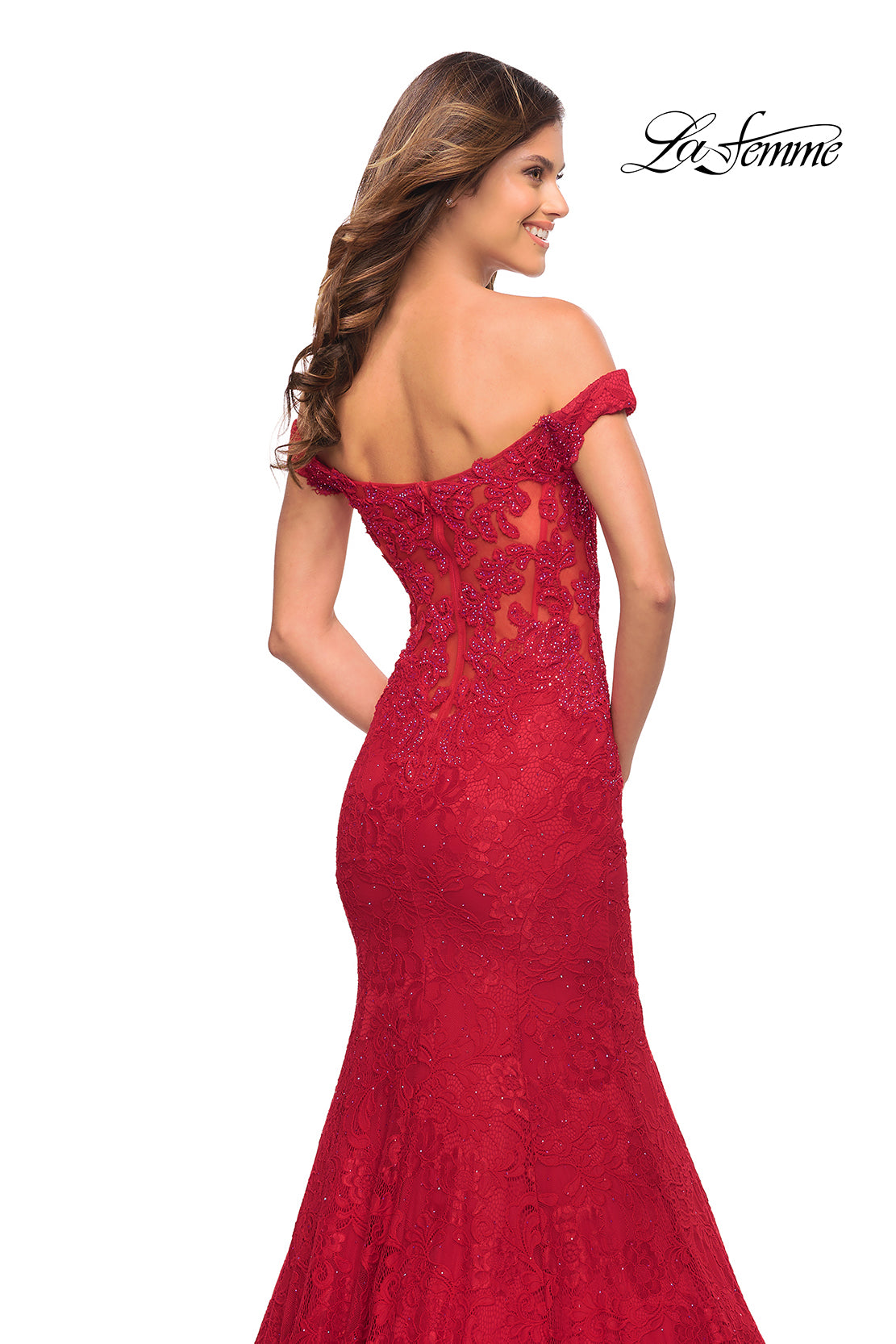 A woman wears the La Femme Off-the-Shoulder Long Lace Prom Dress in red, featuring a fitted sheer back and embroidered details. This elegant, floor-length designer evening gown displays the La Femme logo in the top right corner.